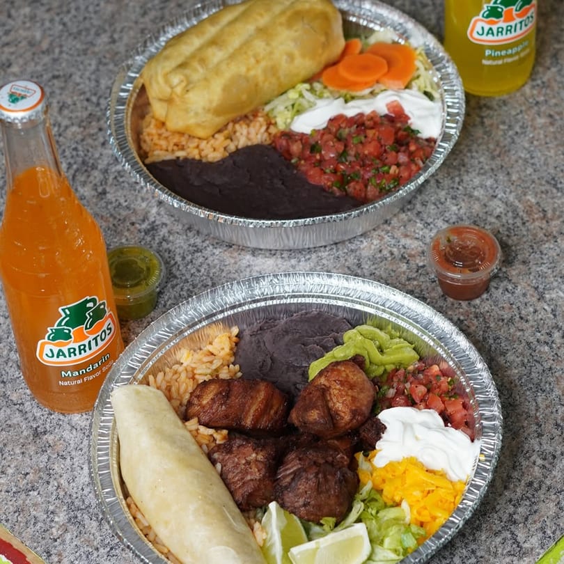 Two Flying Burro Mexican food platters with burritos, rice, beans, and Jarritos sodas.