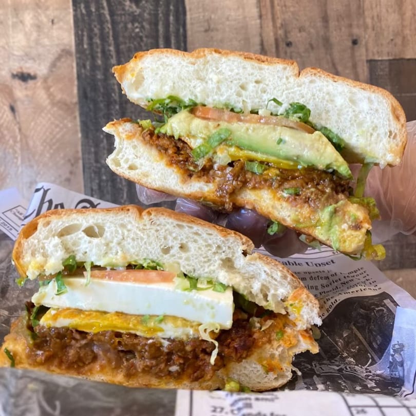 Two halves of a Mexican torta sandwich with chorizo, egg, cheese, avocado, and lettuce.