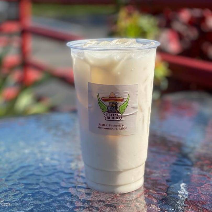 A clear plastic cup of horchata with ice and a Flying Burro sticker sits on a textured table.