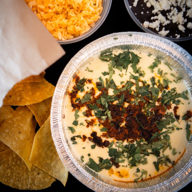 Queso dip with chorizo and cilantro, served with tortilla chips, rice, and black beans.